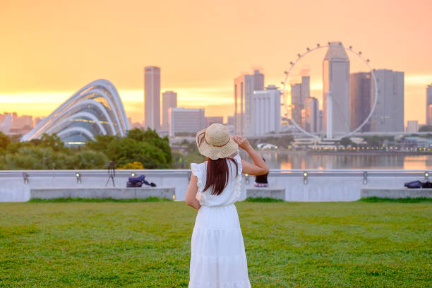 Young Woman traveling with hat at Sunset, happy Asian traveler visit in Singapore city downtown. landmark and popular for tourist attractions. Asia Travel concept